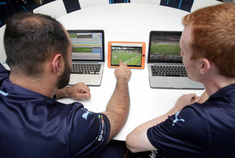 Two soccer players watching videos of gameplay on laptops and tablet