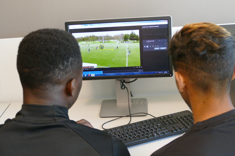 モニターでサッカーの試合映像を分析する 2 人の選手